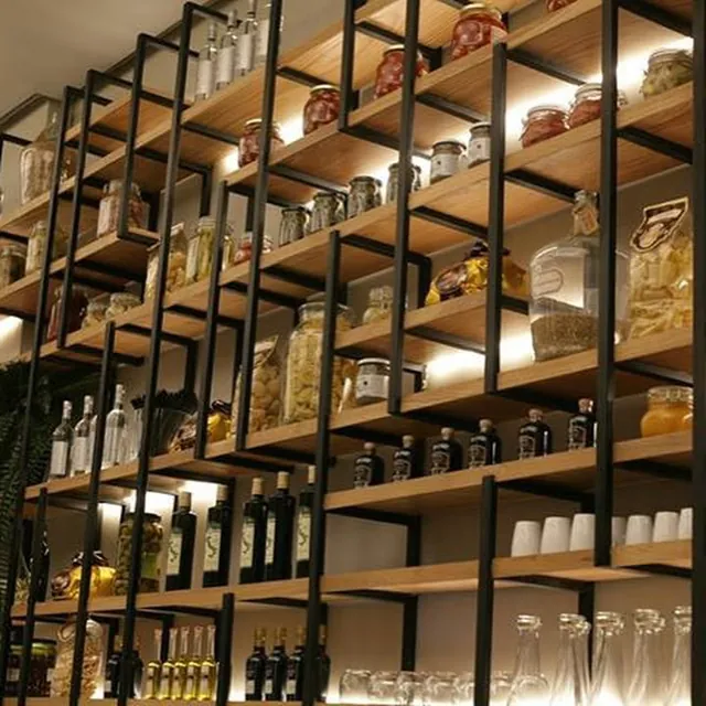 Mur d’étagères en bois et fer chargé de bocaux et de bouteilles