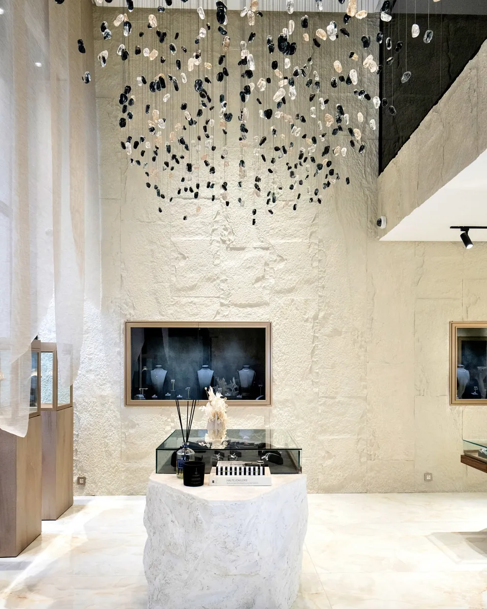 Double hauteur : installation suspendue de perles noires, vitrine encastrée dans un mur de pierre brute