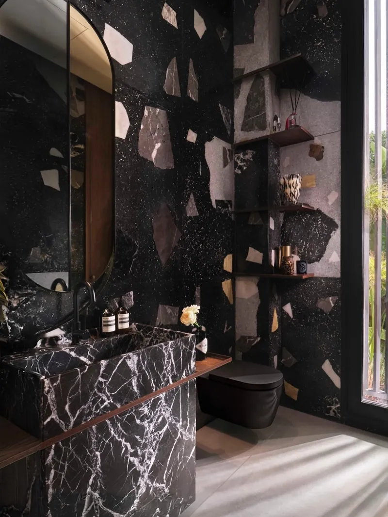 Salle d’eau terminée : vasque en marbre noir veiné de blanc, murs en terrazzo noir aux grands éclats, étagères en acier corten