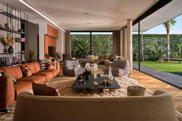 Grand séjour ouvert sur le jardin : canapé cognac, fauteuils zébrés, piliers en béton brut, parquet en chevron