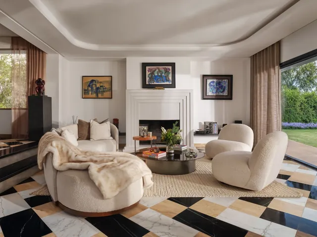 Salon : canapé courbe blanc, fauteuils ronds, cheminée blanche, tableaux