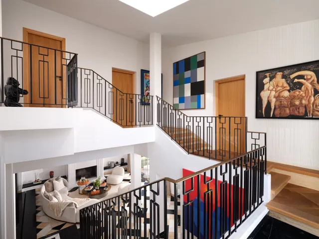 Cage d’escalier : garde-corps en métal noir au dessin Art déco, tableaux colorés
