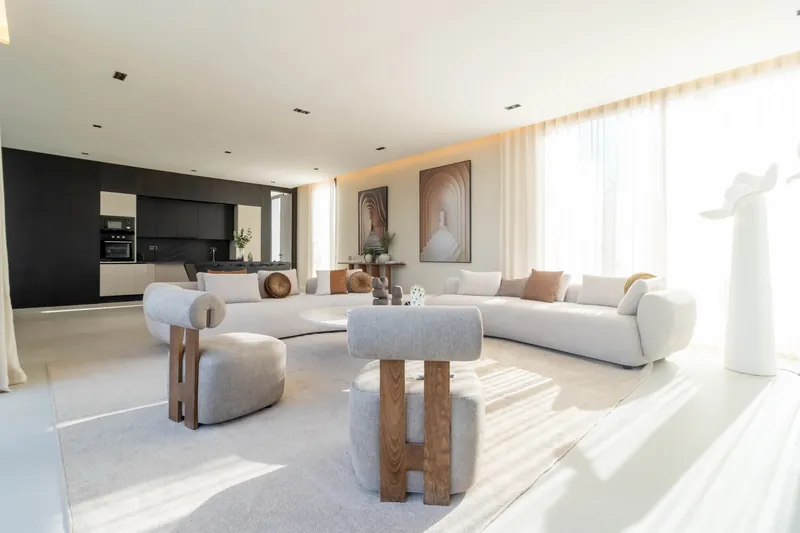 Séjour baigné de lumière : canapé courbe blanc, tables basses rondes, grandes baies sur le jardin